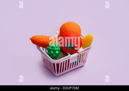 Jouet fruits et légumes dans un panier sur un fond violet avec un espace pour le texte Banque D'Images
