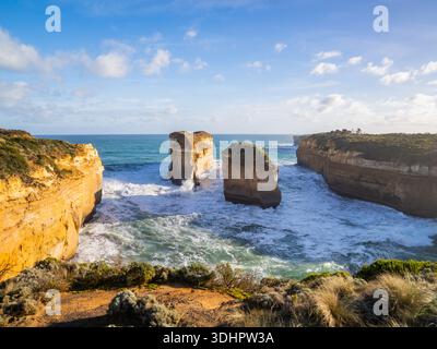 Vue sur les falaises escarpées embrassent la mer turquoise, où la lumière dorée du soleil danse sur les vagues et les anciennes formations rocheuses se dressent haut, Lorne, Victoria, au Banque D'Images