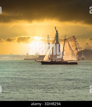 Voilier passant devant la Statue de la liberté au coucher du soleil New York Banque D'Images