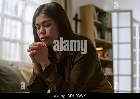 Jeune femme asiatique adulte assise à l'intérieur priant avec les yeux fermés Banque D'Images