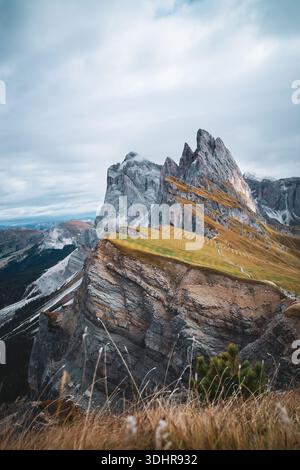 La vue de pics dentelés transperce le ciel, leurs faces rocheuses contrastant avec les pentes douces et herbeuses au premier plan, sous un ciel vaste et nuageux, Urtijei, Banque D'Images