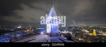 Vue de la tour de l'horloge emblématique illuminée contre le ciel nocturne, debout sur le paysage urbain poussiéreux de neige, une scène pittoresque, Graz, Styrie Banque D'Images