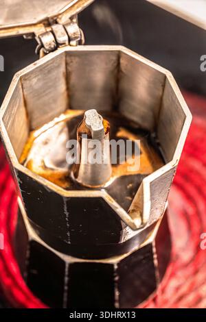 Moka express sur une table de cuisson rouge incandescente commence à préparer du café frais. Banque D'Images