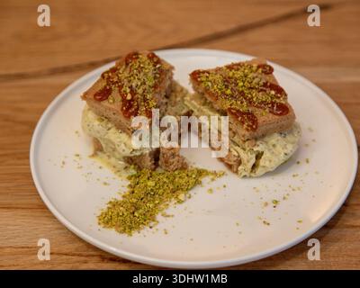 Tranche de dessert en couches de crème glacée à la pistache surmontée de pistache écrasée sur une assiette blanche, photographie de dessert sur une table en bois, vue de face. Banque D'Images