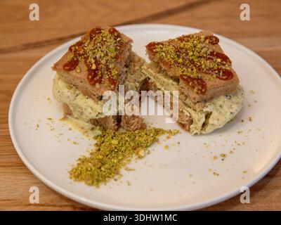 Tranche de dessert en couches de crème glacée à la pistache surmontée de pistache écrasée sur une assiette blanche, photographie de dessert sur une table en bois, vue de face. Banque D'Images
