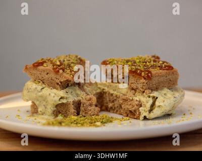 Tranche de dessert en couches de crème glacée à la pistache surmontée de pistache écrasée sur une assiette blanche, photographie de dessert sur une table en bois, vue de face. Banque D'Images