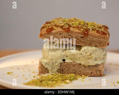 Tranche de dessert en couches de crème glacée à la pistache surmontée de pistache écrasée sur une assiette blanche, photographie de dessert sur une table en bois, vue de face. Banque D'Images