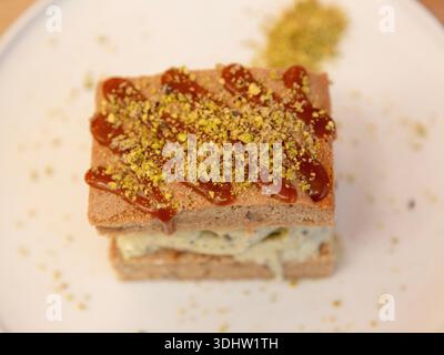 Tranche de dessert en couches de crème glacée à la pistache surmontée de pistache écrasée sur une assiette blanche, photographie de dessert sur une table en bois, vue de face. Banque D'Images