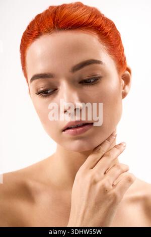 Une jeune femme aux cheveux roux frappants et au maquillage subtil respire la confiance et le style. Banque D'Images