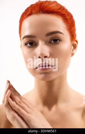 Jeune femme respire la beauté avec des cheveux roux frappants et un maquillage subtil sur une toile de fond unie. Banque D'Images