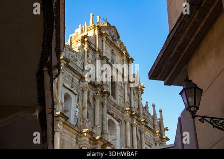 Vue en bas angle sur les ruines de la façade du Groupe Paul à Macao, présentant une architecture baroque en pierre sous un ciel bleu clair encadré par des bâtiments de la ville. Banque D'Images