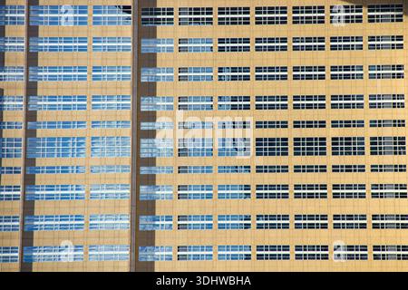 Façade moderne de bâtiment d'entreprise avec une grille répétitive de fenêtres reflétant un ciel bleu et des nuages blancs dans une vue architecturale symétrique. Banque D'Images