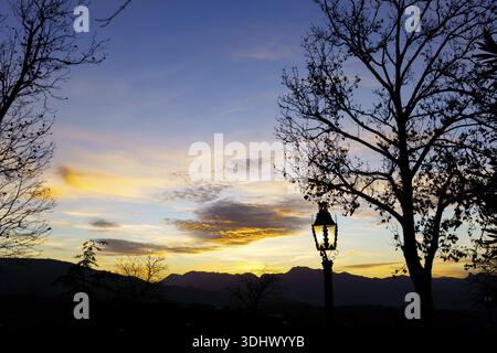 Ronda, malaga, espagne silhouette d'arbres et lampadaire vintage incandescent contre le ciel coloré du coucher du soleil avec des montagnes et des nuages Banque D'Images