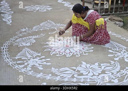 Agartala, Tripura, Inde, 12-01-2026 : des femmes peignent Alpona, sur le terrain avant le festival hindou Makar Sankranti dans le village de Lankamura à Agartala. Banque D'Images