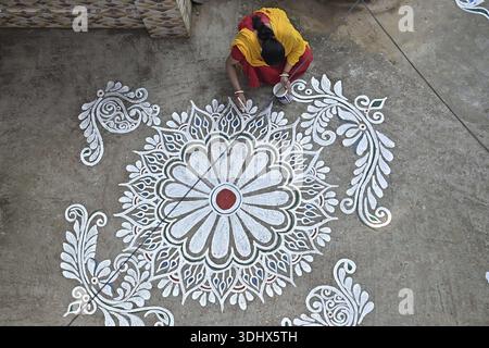 Agartala, Tripura, Inde, 12-01-2026 : des femmes peignent Alpona, sur le terrain avant le festival hindou Makar Sankranti dans le village de Lankamura à Agartala. Banque D'Images