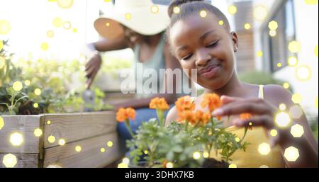 Inspectant la fille touchant des fleurs oranges à la jardinière de patio, femme portant chapeau de soleil tendant à la truelle Banque D'Images