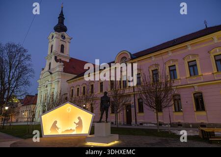 Une scène de soirée sereine dans une ville européenne avec une nativité illuminée par des étoiles brillantes à l'intérieur d'une lanterne polygonale, située contre un bâtiment historique rose avec un Banque D'Images