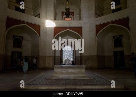 Delhi, Inde - 30 mars 2024 : L'image montre des visiteurs marchant à l'intérieur de la chambre centrale du tombeau de Humayun, avec le cénotaphe principal en marbre, des alcôves voûtées et une fenêtre décorative en treillis éclairée par la lumière du soleil. Banque D'Images
