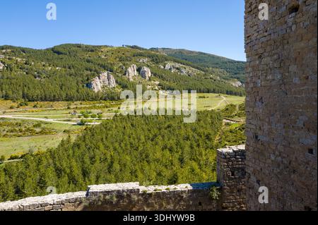Loarre, Espagne - 8 mai 2024 : la campagne et les collines boisées sont visibles depuis le mur de pierre du château de Loarre, avec une section du mur du château au premier plan et des affleurements rocheux en arrière-plan sous un ciel bleu clair. Banque D'Images