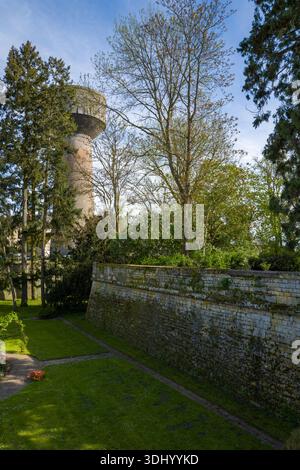 Lieu inconnu - 13 avril 2024 : L'image montre un haut château d'eau en béton s'élevant au-dessus des arbres, avec un mur de soutènement en pierre recouvert de mousse et un jardin paysager avec pelouses et allées au premier plan. Banque D'Images