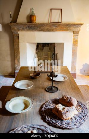 Intérieur rustique avec table à manger en bois cheminée en pierre lumière chaude atmosphère traditionnelle objets vintage style maison de campagne confortable Banque D'Images