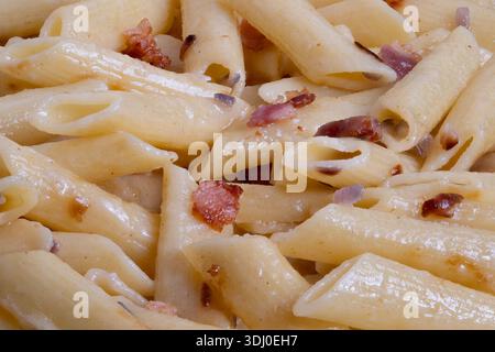 Pâtes penne instantanées garnies de bacon croustillant et d'huile d'olive, pâtes penne préparées rapidement combinées à de petits morceaux de bacon et à un enrobage d'huile savoureux Banque D'Images