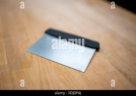 Grattoir de banc reposant sur un comptoir en bois dans une cuisine professionnelle, symbolisant les traditions culinaires italiennes classiques et la préparation du handmad Banque D'Images