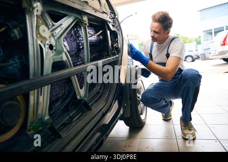 Mécanicien réparer la voiture, en utilisant du mastic en plastique, préparer la surface pour la peinture par pulvérisation Banque D'Images