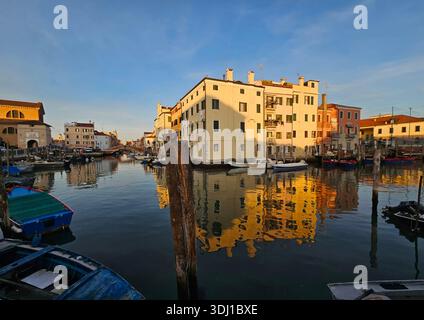 Une scène de canal tranquille sur l'île de Chioggia le long de la côte Adriatique italienne, illuminée par le soleil chaud de fin d'après-midi, mettant en évidence les bâtiments historiques, c Banque D'Images