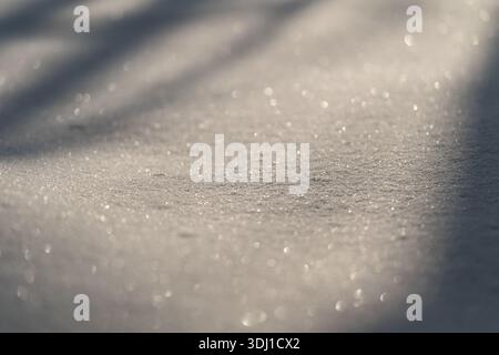 Surface de neige étincelante avec bokeh doux, délicats flocons cristallins captant la lumière du matin. De subtiles lignes d'ombre traversent une pente poudreuse, créant un calme Banque D'Images