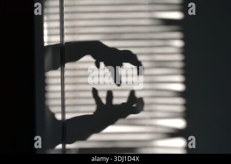 Le jeu de lumière et d'ombre de la lumière du soleil sur le mur. La silhouette des mains, les ombres des mains avec les doigts serrés contre l'ombre des aveugles Banque D'Images