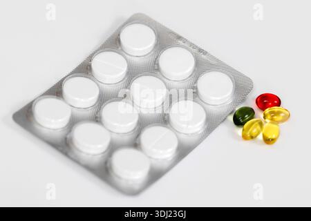 Plaquette thermoformée contenant des comprimés blancs placés à côté de capsules de gel colorées sur une surface blanche propre, mettant en évidence différentes formes et couleurs de médicaments Banque D'Images