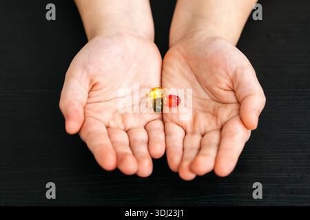 Les mains montrent trois capsules de gélatine de couleurs jaune, verte et rouge, placées sur une surface en bois foncé, soulignant les couleurs vibrantes des suppléments Banque D'Images
