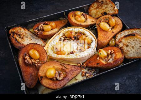 camembert cuit au four avec poires glacées caramélisées, noix et raisins et baguette servie sur une assiette en métal rustique Banque D'Images