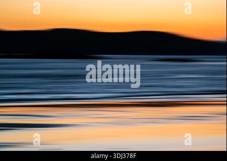 Un paysage marin serein au coucher du soleil présente des stries horizontales d'orange chaud, de bleu profond et de gris doux, créant un effet abstrait et peint. Le m flou Banque D'Images