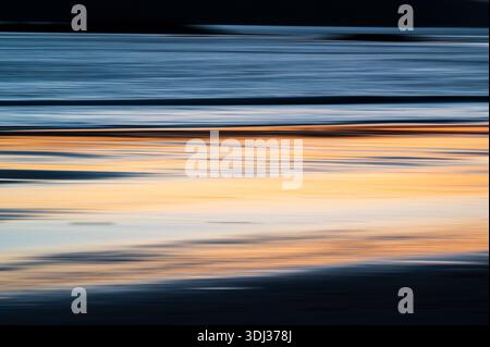 Un paysage marin serein au coucher du soleil présente des stries horizontales d'orange chaud, de bleu profond et de gris doux, créant un effet abstrait et peint. Le m flou Banque D'Images