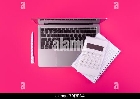 Photo vue de dessus du stylo de calculatrice blanc et cahier sur ordinateur portable gris sur fond rose isolé Banque D'Images