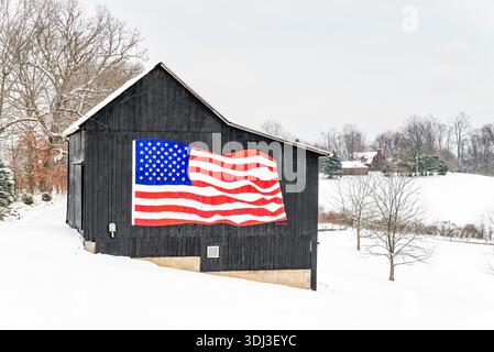 Une fresque du drapeau américain couvrait le côté d'une grange rustique peinte en noir sur une ferme rurale de Pennsylvanie, située contre des champs enneigés un jour d'hiver. Banque D'Images