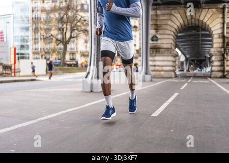 Athlète masculin afro-américain courant sur une piste pavée dédiée sous le pont emblématique de bir hakeim à paris, en se concentrant sur le fitness urbain et une bonne santé Banque D'Images