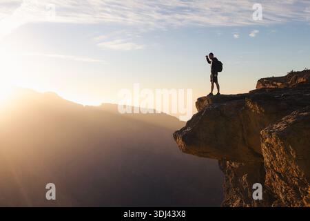Touriste avec sac à dos debout sur le bord de la falaise surplombant le canyon profond à Jebel Akhdar, Oman. Paysage dramatique et sens de l'échelle représentant Adventu Banque D'Images