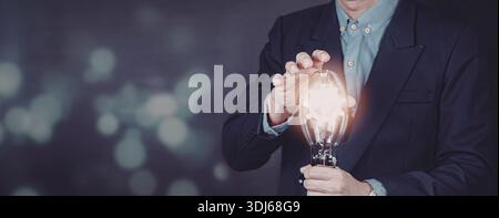 Un homme d'affaires professionnel dans un costume tient une ampoule qui est allumée, symbolisant les idées, l'innovation et l'illumination. Banque D'Images