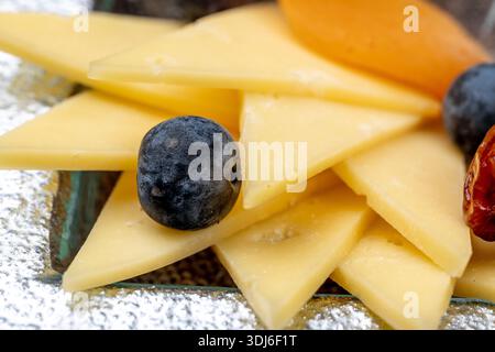 Gros plan d'un élégant hors-d'œuvre composé d'une variété de fromages à pâte dure et molle tranchés, accompagnés de myrtilles, de fruits physalis, de bière rouge séchée Banque D'Images