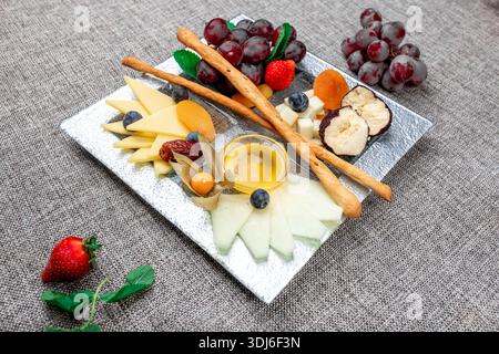 Un plateau de fromage gastronomique magnifiquement arrangé avec différents types de fromage tranché, raisins rouges, fraises fraîches, bleuets, physalis, et dri Banque D'Images