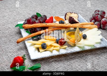 Un plateau de fromage gastronomique magnifiquement arrangé avec différents types de fromage tranché, raisins rouges, fraises fraîches, bleuets, physalis, et dri Banque D'Images