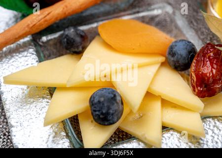 Gros plan d'un élégant hors-d'œuvre composé d'une variété de fromages à pâte dure et molle tranchés, accompagnés de myrtilles, de fruits physalis, de bière rouge séchée Banque D'Images
