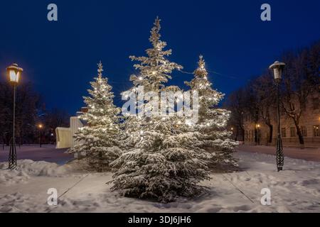 Oulianovsk, Russie - 14 février 2022 : un arbre de Noël enneigé décoré de guirlandes un soir d'hiver. Rue enneigée à Noël déc Banque D'Images