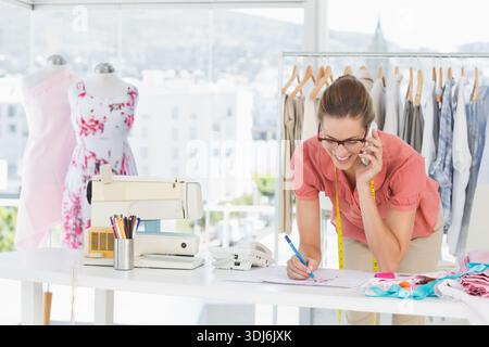 Femme créatrice de mode penchée sur le bureau dans le studio de dessin et portant le ruban à mesurer, espace de copie. Atelier, couturière, couture, dressform, vêtements, Banque D'Images