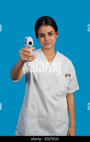 Travailleuse de la santé vérifiant la température corporelle avec un thermomètre sans contact sur fond bleu Banque D'Images