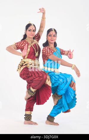 Deux danseuses bharatanatyam interprétant des poses de danse indienne classique en costume traditionnel et bijoux, photographiées dans un studio contre un blanc Banque D'Images