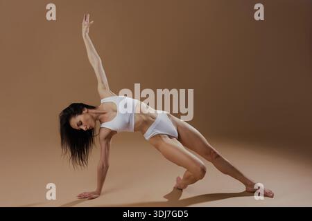 Forte femme athlétique faisant la pose d'équilibre de yoga dans un cadre de studio minimal, montrant la forme physique et la flexibilité. Banque D'Images